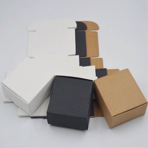 K&ouml;nnte beinhalten: Drei kleine Geschenkboxen in Wei&szlig;, Schwarz und Braun. Die Boxen sind aus Pappe und haben ein schlichtes, minimalistisches Design.