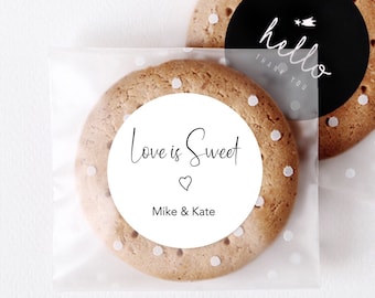 May include: Two clear cellophane bags with white polka dots. One bag contains a cookie with a white circle sticker that says "Love is Sweet" with a heart and "Mike & Kate". The other bag contains a cookie with a black circle sticker that says "hello thank you".