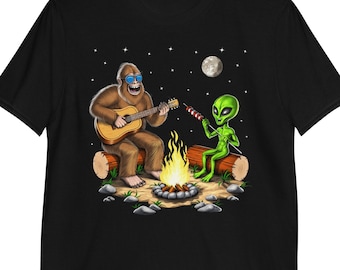 Könnte beinhalten: Ein schwarzes T-Shirt mit einem Aufdruck eines Bigfoots, der Gitarre spielt, und einem Außerirdischen, der einen Spieß mit Essen in der Hand hält, am Lagerfeuer unter einem sternenklaren Nachthimmel.