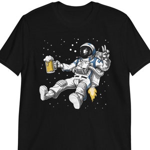 May include: A black t-shirt with a graphic of an astronaut floating in space with a beer in hand. The astronaut is wearing a white spacesuit with blue accents and a jetpack. The background is a dark blue space with stars.