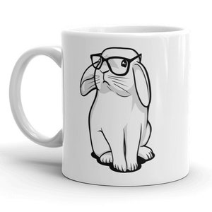 May include: White ceramic coffee mug with a black and white illustration of a rabbit wearing glasses.