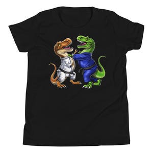 May include: Black youth t-shirt featuring a green and brown dinosaur wearing a blue karate uniform and a brown dinosaur wearing a white karate uniform.