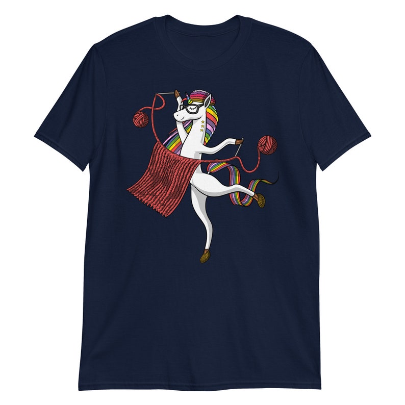 Puede incluir: Una camiseta azul marino con un unicornio blanco que lleva gafas y teje una bufanda roja. El unicornio tiene una melena y una cola arco&iacute;ris.