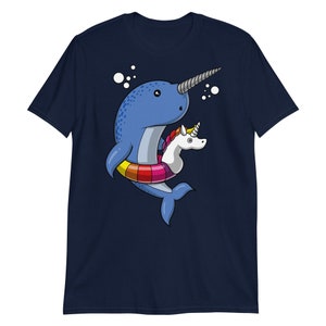 May include: A navy blue t-shirt with a cartoon illustration of a narwhal wearing a rainbow inflatable ring with a unicorn riding on top.