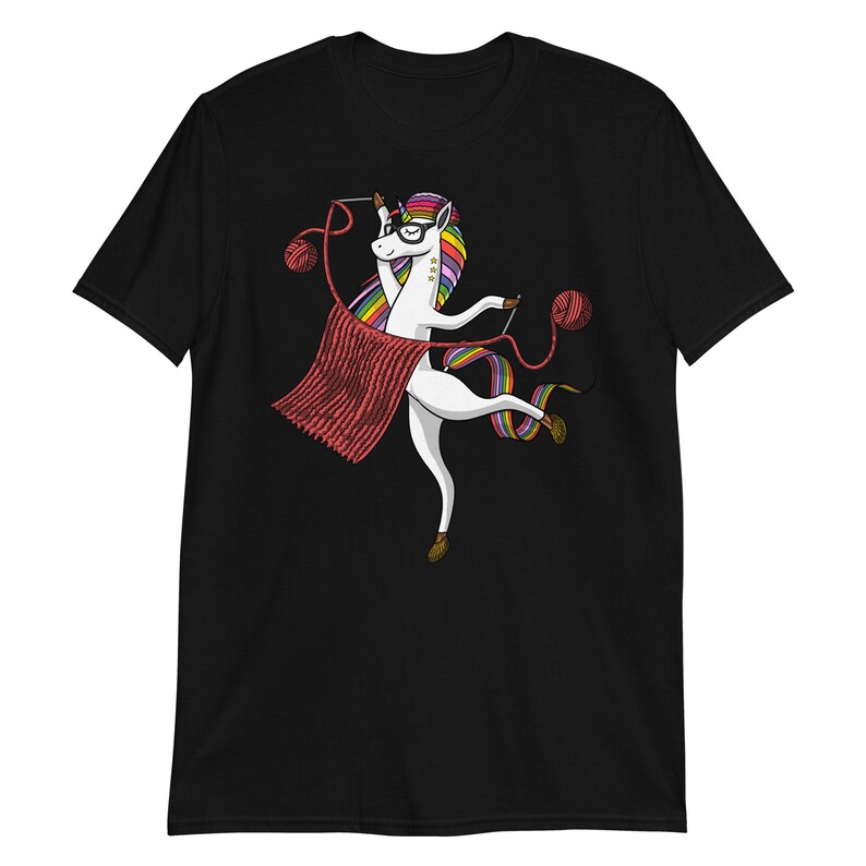 Puede incluir: Una camiseta negra con un unicornio blanco que lleva gafas y teje una bufanda roja. El unicornio tiene una melena y una cola arco&iacute;ris.