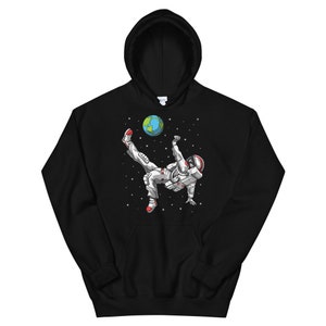 May include: Black hooded sweatshirt with a graphic of an astronaut kicking a soccer ball that is the Earth. The astronaut is wearing a white spacesuit with red accents.