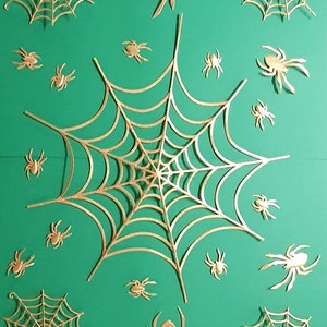 May include: A green background with gold glitter spiderwebs and spiders. The spiderwebs are intricate and detailed, and the spiders are all different sizes.