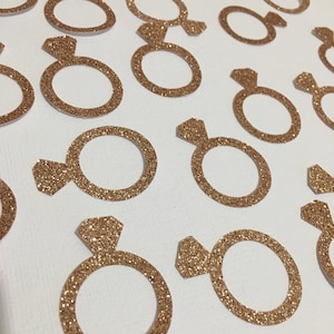 Puede incluir: Una colecci&oacute;n de confeti en forma de anillo de color dorado con purpurina, ideal para a&ntilde;adir un toque de brillo a la decoraci&oacute;n de una boda o una despedida de soltera.