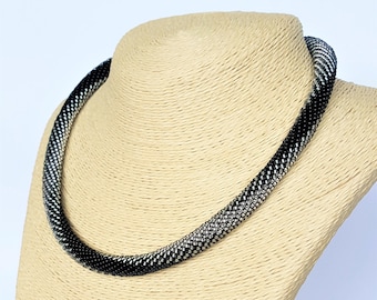 May include: A black and silver beaded necklace on a beige mannequin bust. The necklace is made of small, round beads that are arranged in a graduated pattern, with the black beads at the bottom and the silver beads at the top.