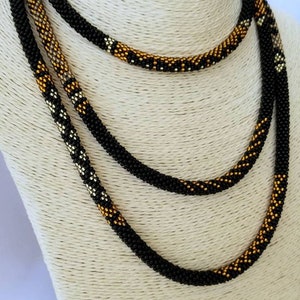 May include: A multi-strand beaded necklace with black, gold, and silver beads. The necklace is layered and has a geometric pattern.