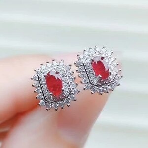 May include: A pair of silver earrings with a red oval gemstone surrounded by smaller clear gemstones.