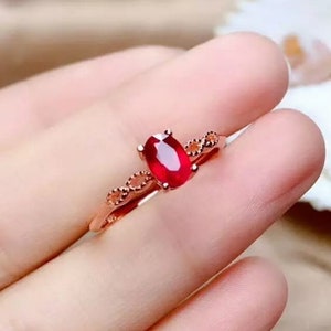 Peut inclure: Une bague avec une pierre ovale rouge sertie dans une délicate bande dorée. La bande est ornée d'un motif décoratif.
