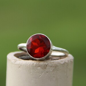 May include: A silver ring with a large, round, red gemstone.