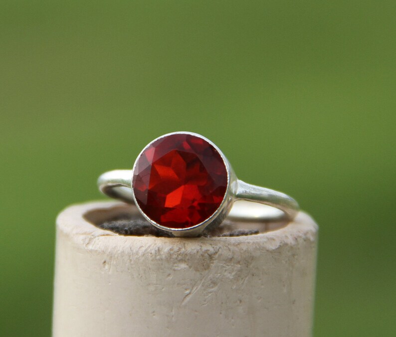May include: A silver ring with a large, round, red gemstone.