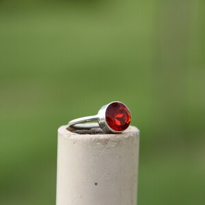 May include: A silver ring with a large, round, red gemstone.
