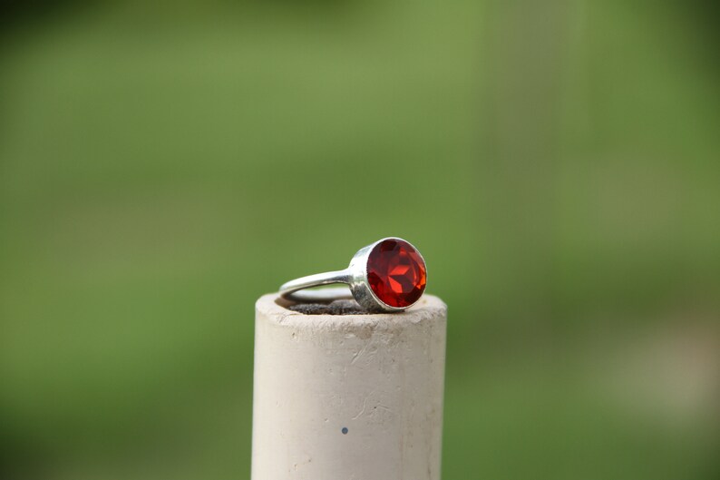 May include: A silver ring with a large, round, red gemstone.