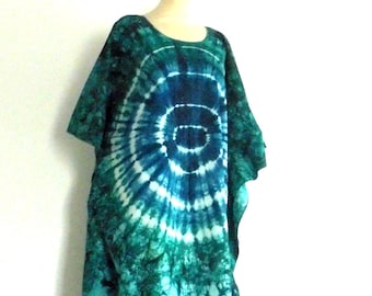 May include: A floor-length kaftan featuring a tie-dye pattern in shades of deep blue, teal, and emerald green. The garment has a round neckline, short sleeves, and a loose, flowing silhouette with two prominent circular spiral motifs.