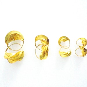May include: Four gold hoop earrings of varying sizes. The earrings are made of twisted metal and have a leaf-like design.