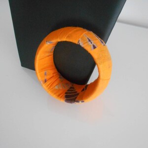 Könnte beinhalten: Orangefarbenes Stoffarmband mit einem lila-weißen Muster.