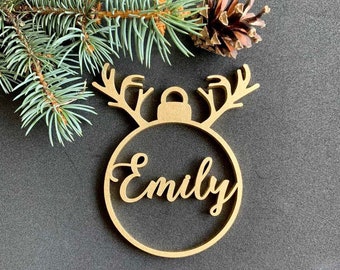 May include: Gold wooden Christmas ornament shaped like a reindeer with antlers and a circle with the name "Emily" cut out.