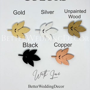 May include: A sample of different colors of wooden leaves, including gold, silver, unpainted wood, black, and copper. The leaves are arranged in a row, with the text "COLORS" above them and "BETTER WEDDING DECOR" below them.