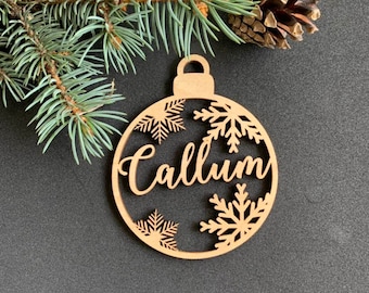 May include: A wooden Christmas ornament shaped like a bauble with the name "Callum" cut out and snowflakes around the name.