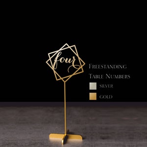 May include: Gold freestanding table number with a geometric design and the number "four" in cursive script. The table number is on a gold stand. The image also shows a color chart with silver and gold options.