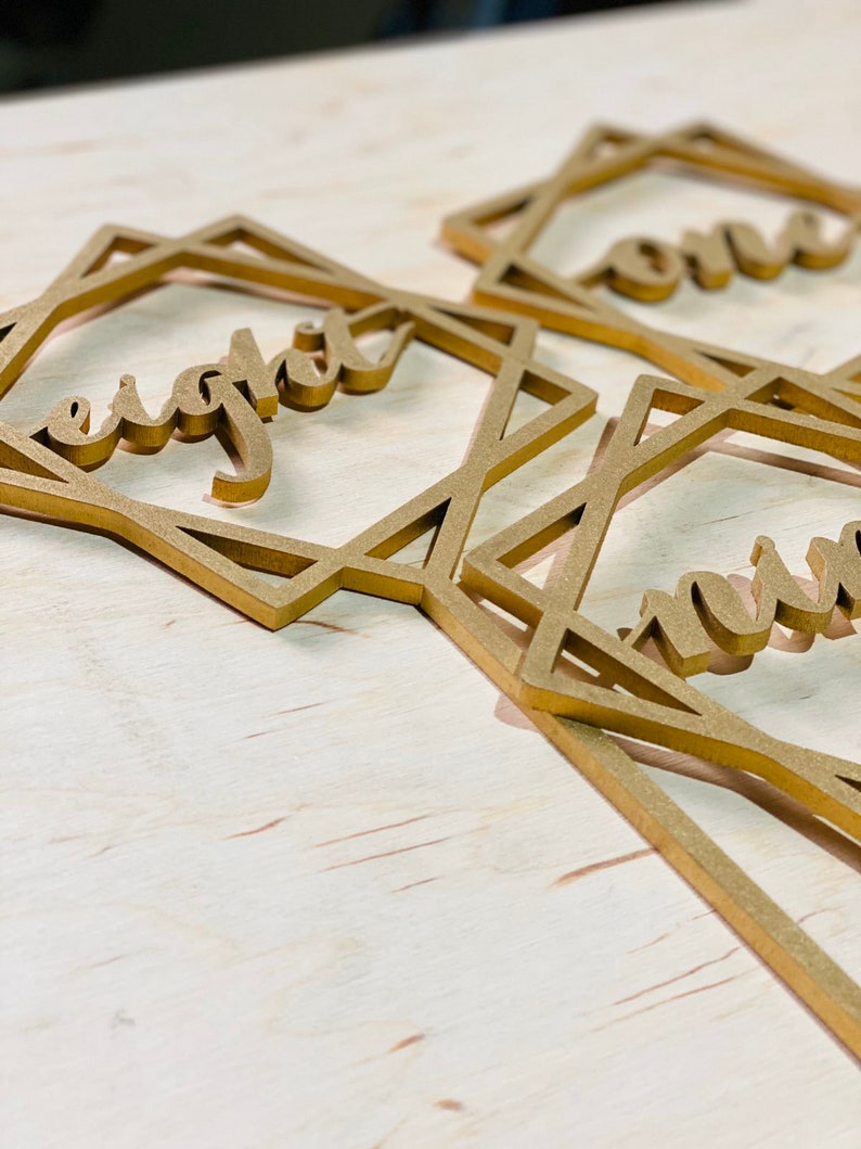 May include: Three gold geometric frames with the words "one", "eight", and "nine" written inside. The frames are made of wood and have a rustic look.