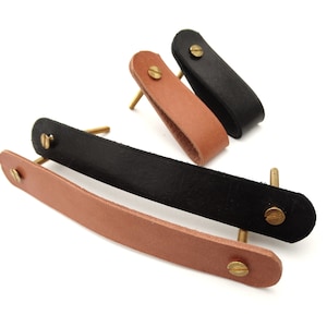 Puede incluir: Tres tiradores de armario de cuero con tornillos de latón. Dos son marrones y uno es negro.