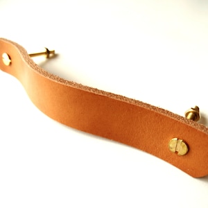 Peut inclure: Une poignée de tiroir en cuir marron avec deux vis en laiton.