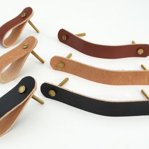 Op de afbeelding: Zes leren kastgrepen met messing schroeven. De grepen zijn in drie kleuren: bruin, zwart en naturel.