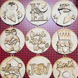 May include: Nine wooden Christmas ornaments with various designs. The ornaments feature a gingerbread person, snowman, Santa Claus, reindeer, nutcracker, and the words "Noel", "Jingle All The Way", and "Joy".