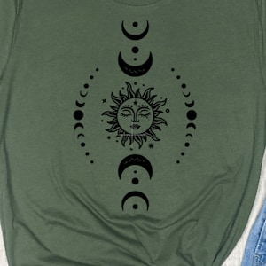 May include: A green t-shirt with a black sun and moon design. The sun has a face and is surrounded by stars. The moon is in various phases.