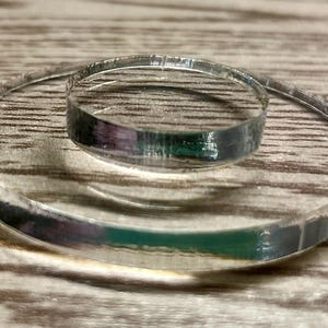 May include: Two clear acrylic circles, one smaller than the other, are stacked on top of each other. The circles are on a light brown wooden surface.