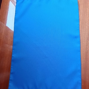 May include: A plain blue fabric pouch with a drawstring closure. The pouch is lying flat on a wooden surface.