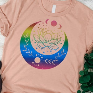 May include: A pink t-shirt with a rainbow crescent moon design featuring a lotus flower and stars.