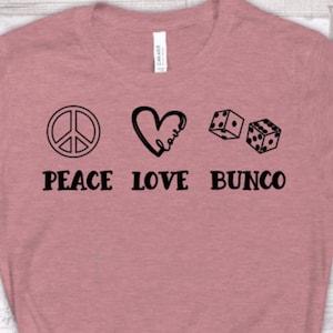 May include: A pink t-shirt with a peace sign, a heart with the word "love" inside, and two dice. The text "Peace Love Bunco" is printed below the images.
