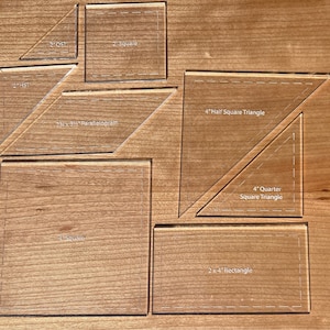 May include: A set of clear acrylic quilting rulers for sewing projects. The rulers include a 4-inch half square triangle, a 4-inch quarter square triangle, a 2-inch square, a 4-inch square, a 2-inch by 4-inch rectangle, a 2-inch by 4-inch parallelogram, and a 2-inch half square triangle.