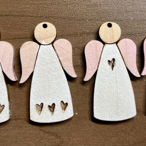 May include: Four wooden angel ornaments with pink wings and white paint. Each angel has a heart design on the front.