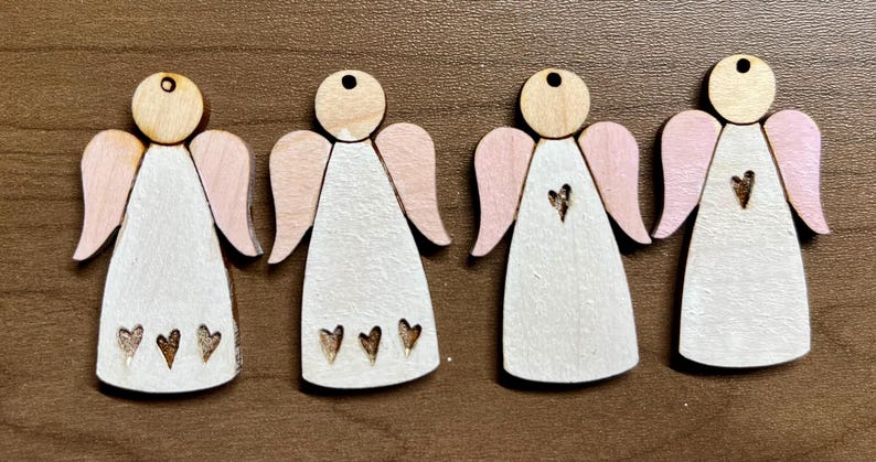 May include: Four wooden angel ornaments with pink wings and white paint. Each angel has a heart design on the front.