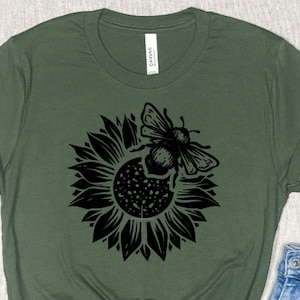 May include: A green t-shirt with a black sunflower and bee graphic. The bee is flying towards the sunflower.