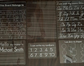 May include: Six clear plastic dry-erase boards with white writing. The boards include the alphabet, cursive letters, numbers, and shapes. One board says "This Board Belongs to" and has a space for a name. Another board says "Hello my name is" and has a space for a name.