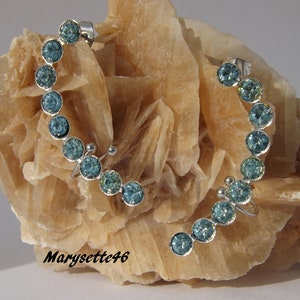Peut inclure: Une manchette d'oreille argentée avec une rangée de strass bleu clair. La manchette est incurvée et se termine par une petite boule argentée.