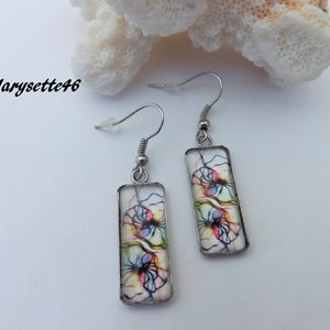 May include: A pair of silver dangle earrings with rectangular glass charms featuring colourful abstract designs. The charms are transparent and show a white background with colourful lines and shapes.