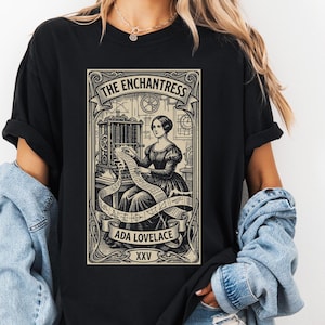 Peut inclure: T-shirt noir avec un graphisme détaillé d'Ada Lovelace, intitulé "The Enchantress". Le design comprend une illustration vintage de Lovelace avec une machine et du texte. Le t-shirt est de style décontracté et confortable.