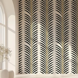Op de afbeelding: Een crèmekleurige muur met een herhalend patroon van zwarte en gouden bladvormige vormen. Het ontwerp is verticaal en creëert een textuureffect. De kamer heeft een groot boogvenster en witte vazen.