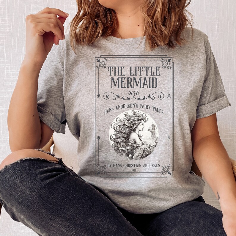 Pu&ograve; includere: Maglietta grigia con un design di copertina di libro vintage con un'illustrazione di sirena e il testo "The Little Mermaid, Hans Andersen's Fairy Tales, By Hans Christian Andersen 1837".