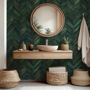 May include: A bathroom interior with a round mirror in a woven frame, a stone sink, and a wooden shelf. The dark green herringbone tiled wall provides a striking backdrop. Woven baskets and a towel add to the natural, spa-like feel.