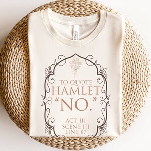 May include: A beige t-shirt with a brown graphic design featuring a quote from Hamlet: "To quote Hamlet "NO." Act III Scene III Line 87"