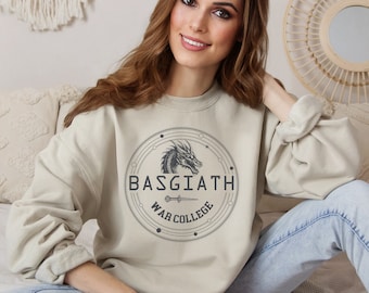 Può includere: Una felpa beige con una grafica in bianco e nero di una testa di drago all'interno di un cerchio. Il cerchio contiene il testo "Basgiath War College".